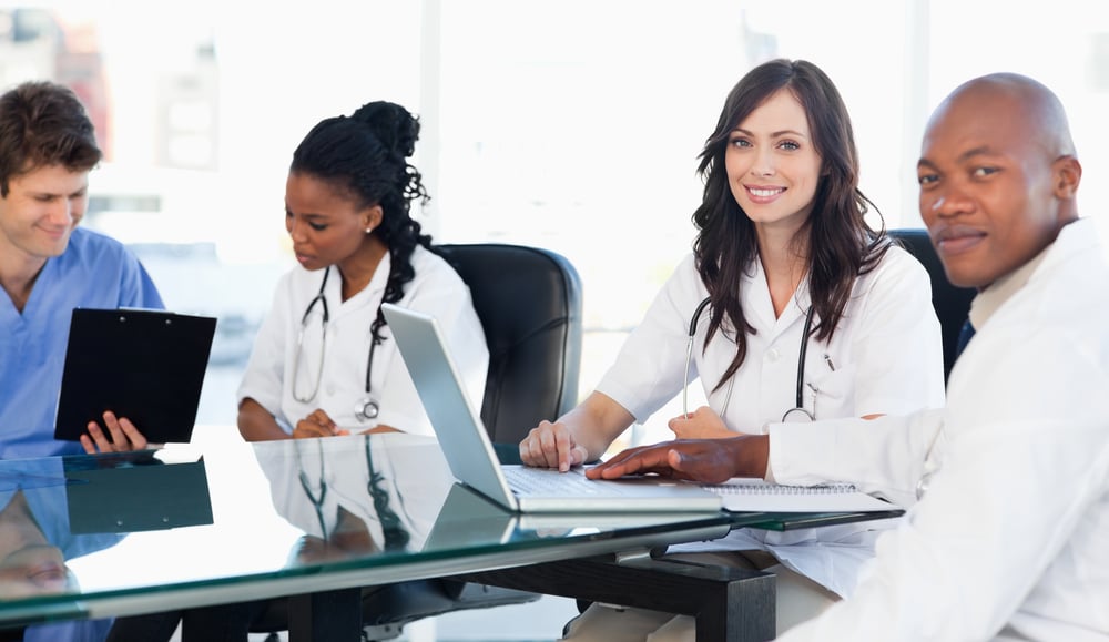 Members of a medical team looking at the camera while working on a laptop Members of a medical team looking at the camera while working on a laptop